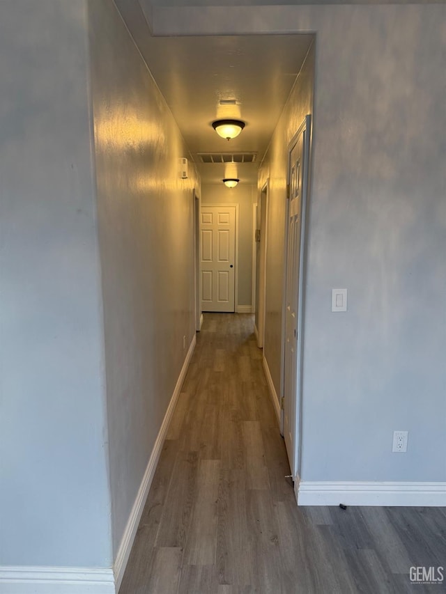 hallway with dark wood-type flooring, visible vents, and baseboards