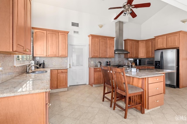 kitchen featuring sink, a breakfast bar area, stainless steel fridge, a kitchen island with sink, and wall chimney range hood