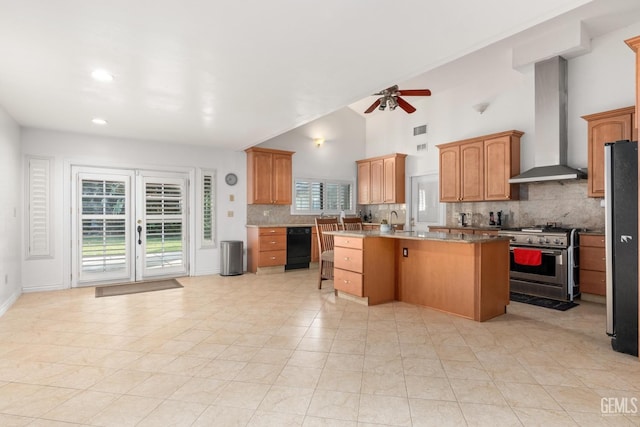 kitchen with wall chimney range hood, ceiling fan, stainless steel appliances, a center island, and tasteful backsplash