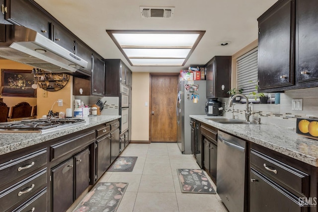 kitchen with light tile patterned floors, sink, dark brown cabinets, stainless steel appliances, and light stone countertops