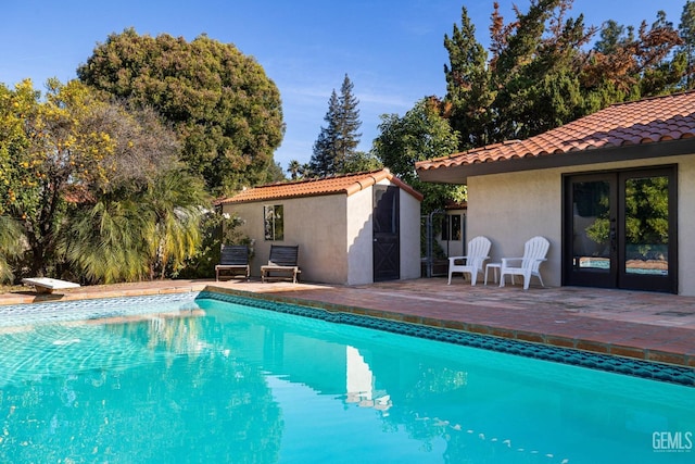 view of pool with a diving board, a patio area, an outbuilding, and french doors