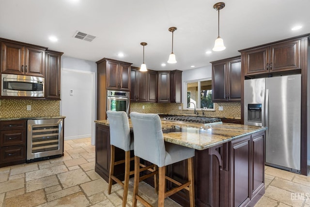 kitchen with a center island, wine cooler, dark stone countertops, pendant lighting, and appliances with stainless steel finishes