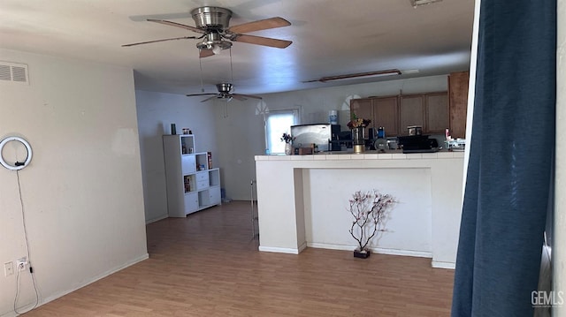 kitchen featuring tile countertops, visible vents, light wood-type flooring, a peninsula, and fridge