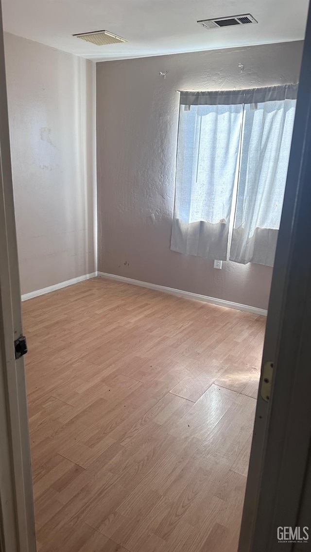 spare room featuring baseboards, visible vents, and wood finished floors