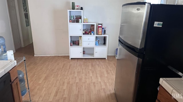 kitchen with tile counters, freestanding refrigerator, and light wood finished floors