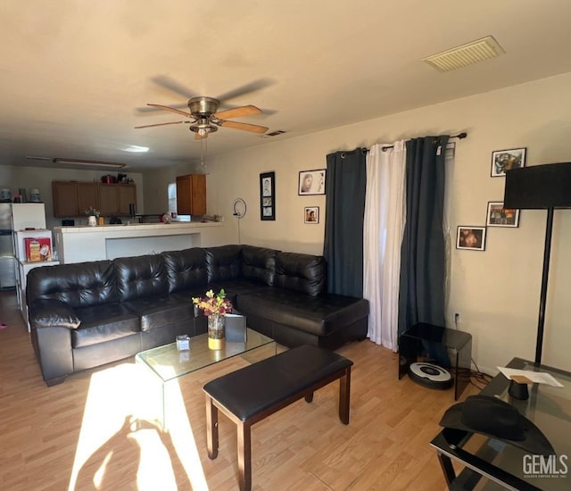 living room with light wood-style flooring, visible vents, and a ceiling fan