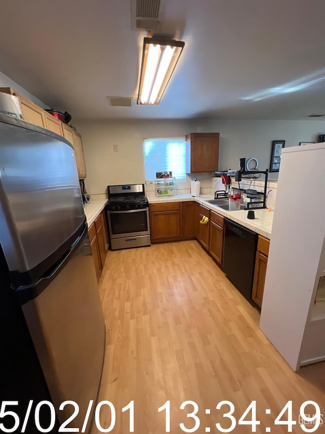 kitchen with stainless steel appliances, visible vents, light countertops, brown cabinets, and light wood finished floors