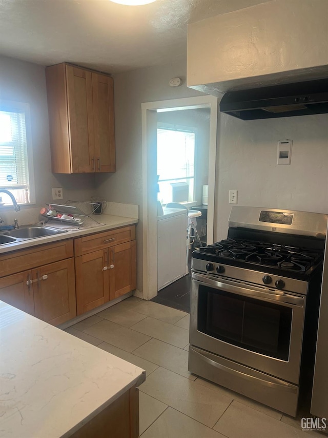 kitchen with stainless steel gas range, brown cabinets, a sink, under cabinet range hood, and light countertops