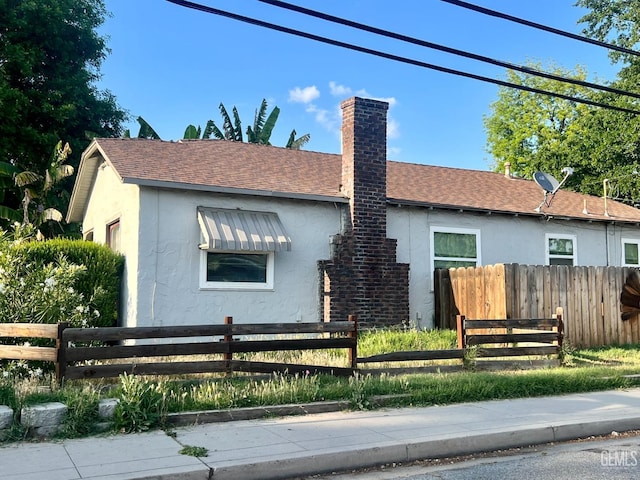 view of front of home with fence private yard, a shingled roof, stucco siding, and a chimney