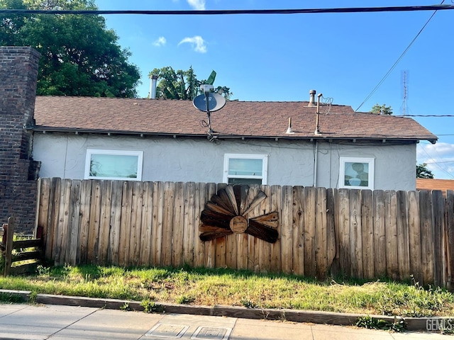 view of side of home with a shingled roof, stucco siding, fence, and ceiling fan