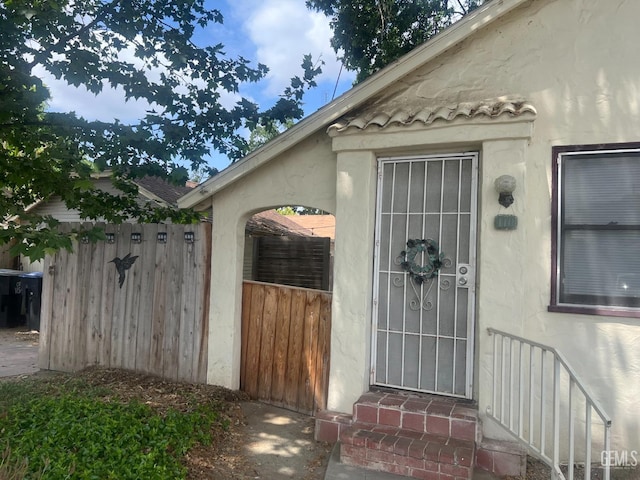 doorway to property featuring fence and stucco siding