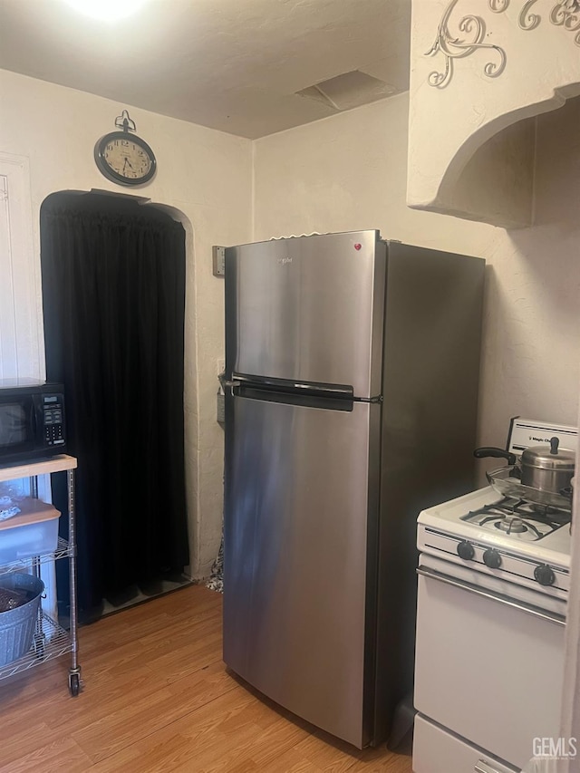 kitchen with freestanding refrigerator, light wood finished floors, black microwave, and white range with gas stovetop