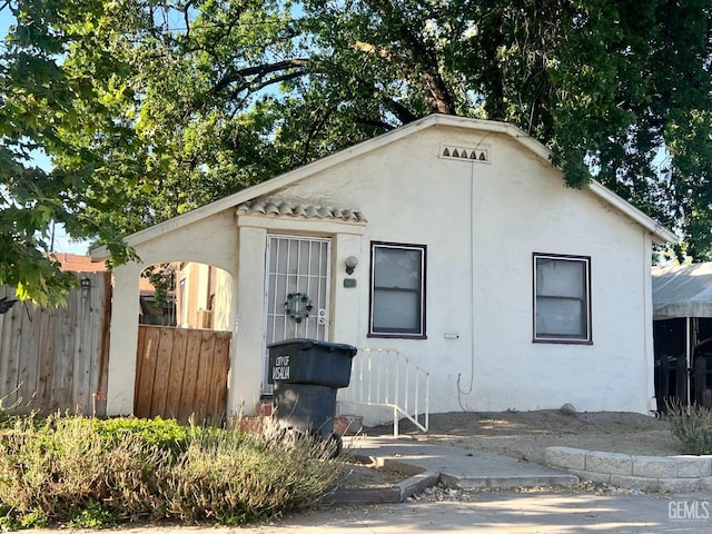 bungalow-style home with stucco siding and fence
