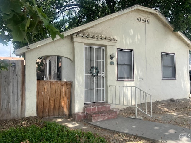 bungalow-style home with stucco siding and fence