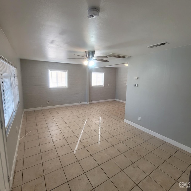 spare room featuring light tile patterned floors, ceiling fan, and brick wall