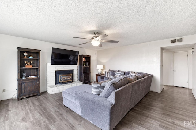 living room with ceiling fan, a fireplace, hardwood / wood-style floors, and a textured ceiling