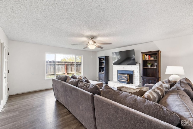 living room featuring a brick fireplace, a textured ceiling, dark wood-type flooring, and ceiling fan