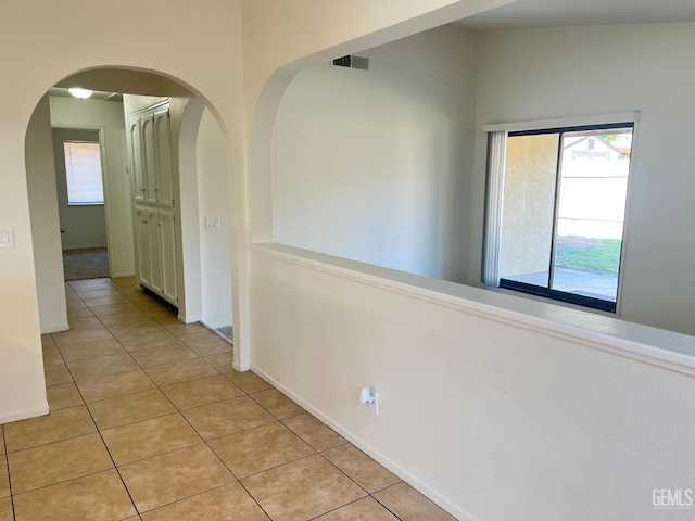 hallway with light tile patterned floors, arched walkways, baseboards, and visible vents