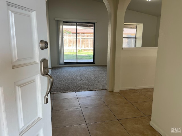 tiled foyer entrance with carpet flooring, arched walkways, and baseboards
