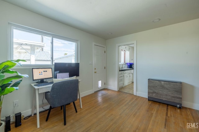 office area featuring baseboards, a sink, a healthy amount of sunlight, and wood finished floors