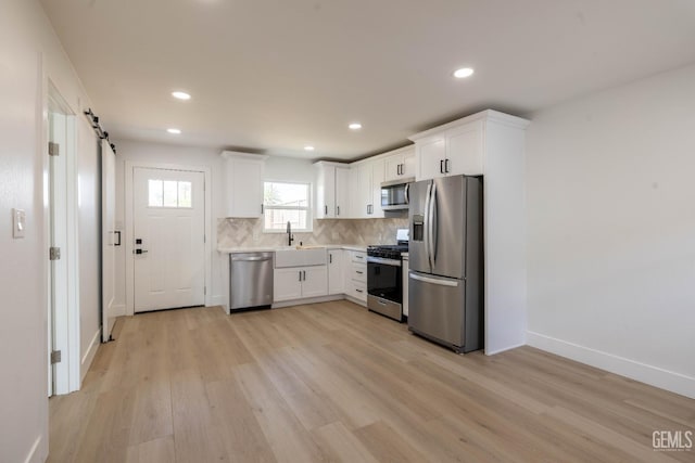 kitchen with a sink, appliances with stainless steel finishes, light wood-style flooring, and white cabinetry