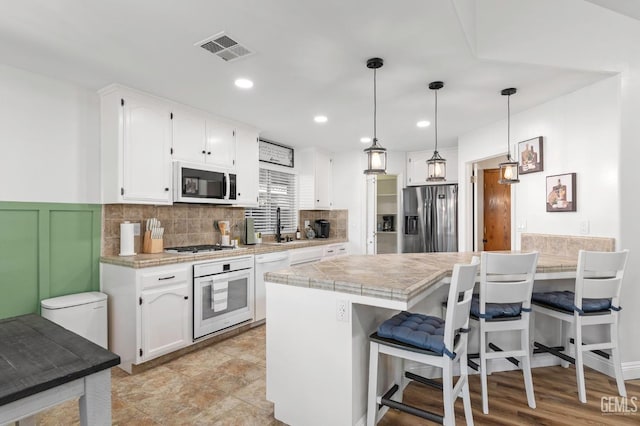 11106 Mohican Dr, Bakersfield, CA 93312 - kitchen with visible vents, a peninsula, white appliances, a kitchen bar, and white cabinetry