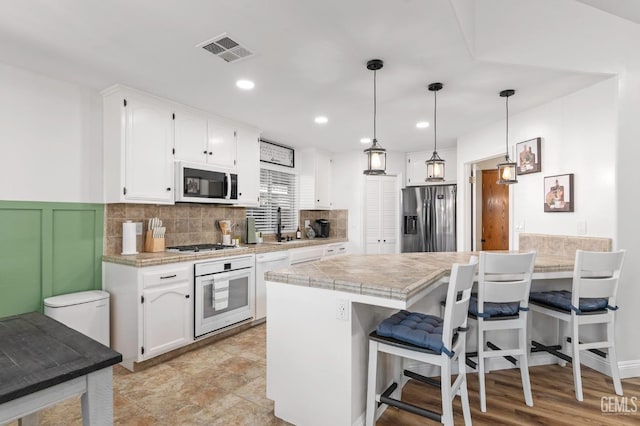 11106 Mohican Dr, Bakersfield, CA 93312 - kitchen featuring visible vents, a peninsula, a breakfast bar, white cabinetry, and appliances with stainless steel finishes
