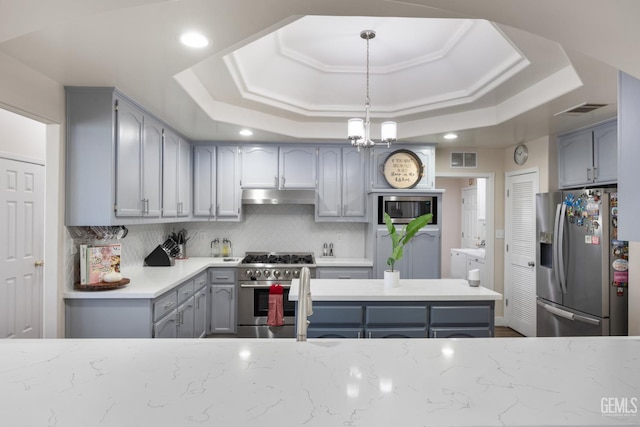 3404 Medallion Rose Ave, Bakersfield, CA 93313 - kitchen with stainless steel appliances, under cabinet range hood, a tray ceiling, gray cabinetry, and backsplash