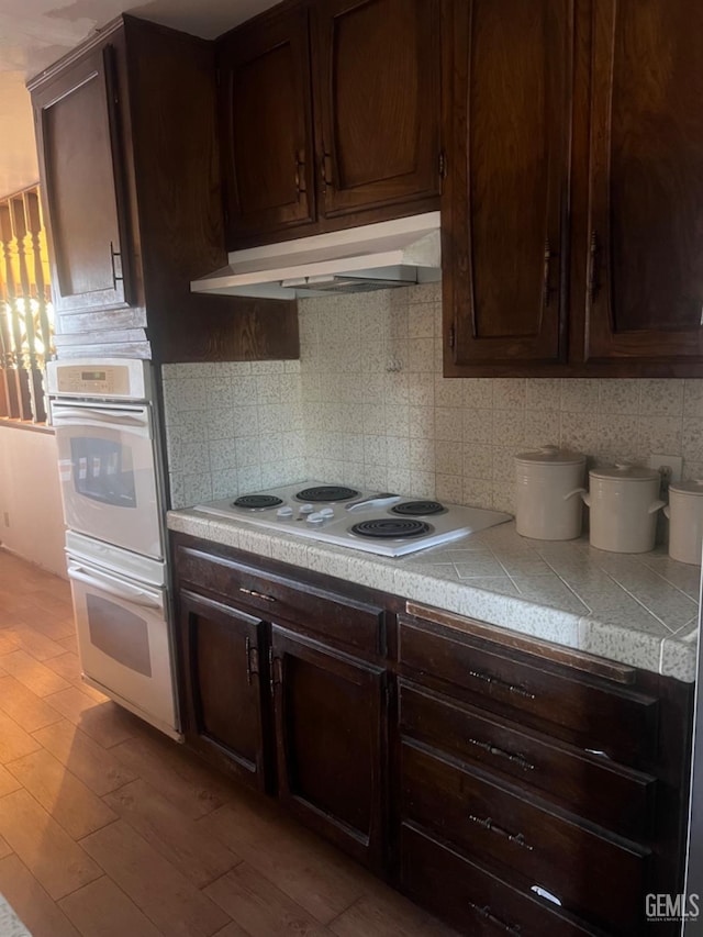 kitchen featuring backsplash, dark brown cabinets, white appliances, and light wood-type flooring