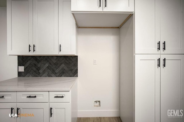 kitchen with tasteful backsplash, light stone counters, white cabinetry, and light hardwood / wood-style floors