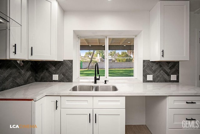 kitchen with decorative backsplash, light stone counters, white cabinetry, and sink