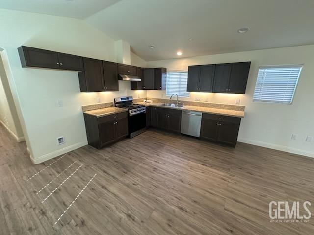 kitchen with appliances with stainless steel finishes, light hardwood / wood-style flooring, lofted ceiling, and sink