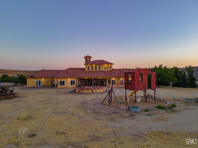 9446 E Kern River Ave, Bakersfield, CA 93308 - back of house at dusk featuring a tile roof, a playground, a chimney, and stucco siding