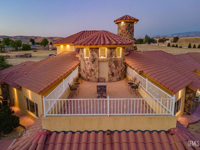 9446 E Kern River Ave, Bakersfield, CA 93308 - back of house at dusk with stone siding, a tile roof, outdoor dining area, a chimney, and stucco siding