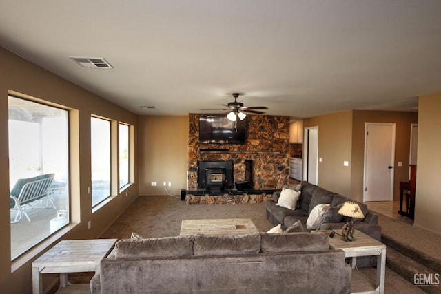 carpeted living room featuring a wood stove and ceiling fan