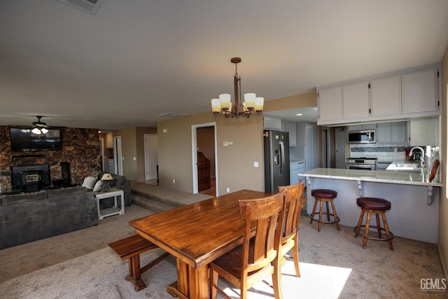 dining room featuring a wood stove, light carpet, sink, and ceiling fan with notable chandelier