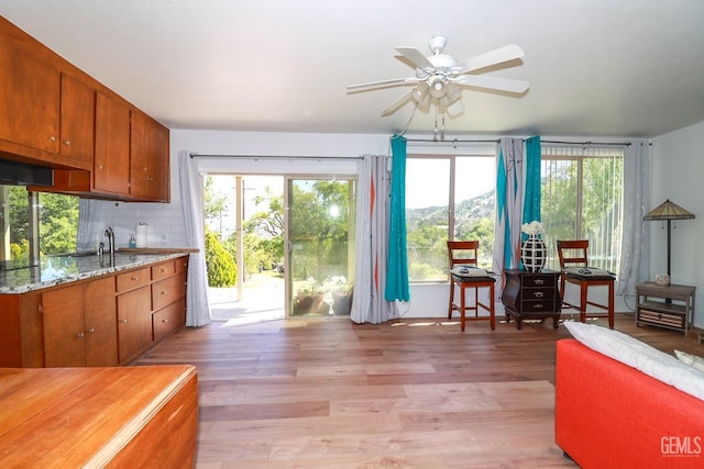 kitchen with decorative backsplash, light hardwood / wood-style floors, light stone countertops, and ceiling fan