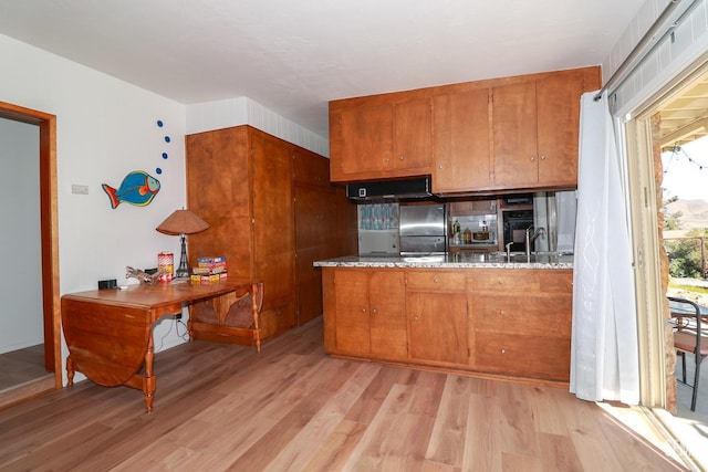 kitchen with stainless steel fridge, light wood-type flooring, light stone counters, and sink