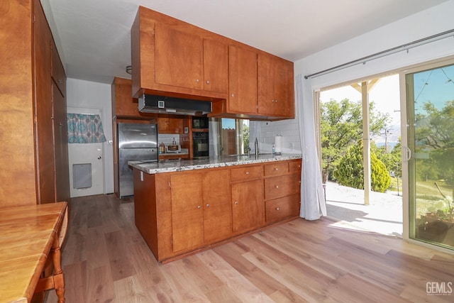 kitchen with light stone countertops, light hardwood / wood-style flooring, black appliances, and sink