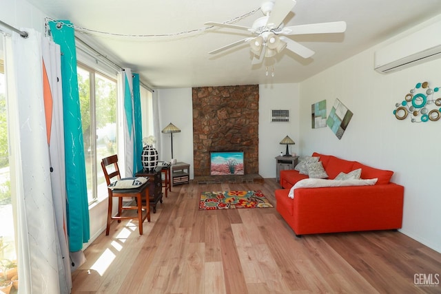 living room featuring hardwood / wood-style flooring, ceiling fan, a stone fireplace, and a wall unit AC