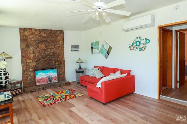 living room with ceiling fan, a stone fireplace, wood-type flooring, and a wall unit AC