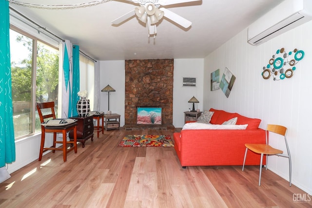 living room with hardwood / wood-style floors, a stone fireplace, a wall mounted AC, and ceiling fan