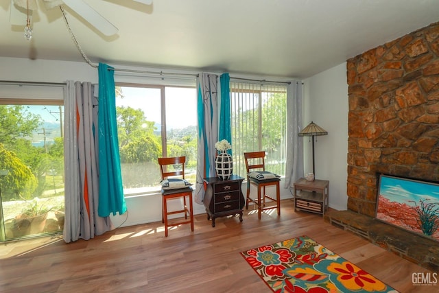 living area featuring hardwood / wood-style floors, a stone fireplace, and ceiling fan