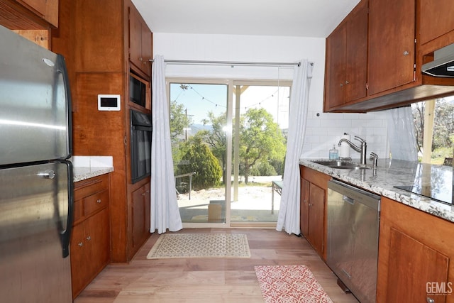 kitchen with black appliances, sink, light hardwood / wood-style flooring, light stone countertops, and tasteful backsplash