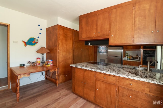 kitchen with black appliances, ventilation hood, sink, light wood-type flooring, and light stone countertops