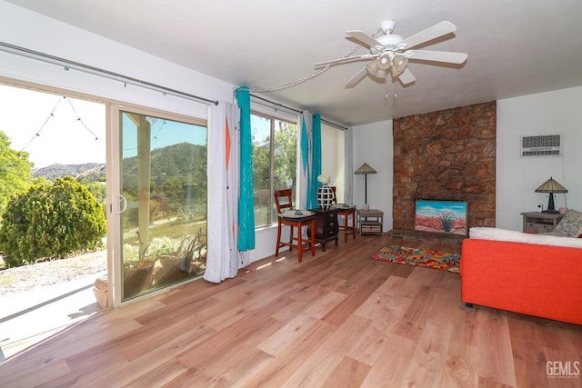 living room with ceiling fan, a stone fireplace, and light hardwood / wood-style flooring