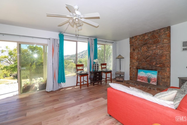 living room featuring ceiling fan, a stone fireplace, light wood-type flooring, and a mountain view