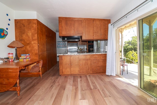 kitchen featuring ventilation hood, light stone countertops, light hardwood / wood-style floors, kitchen peninsula, and stainless steel refrigerator