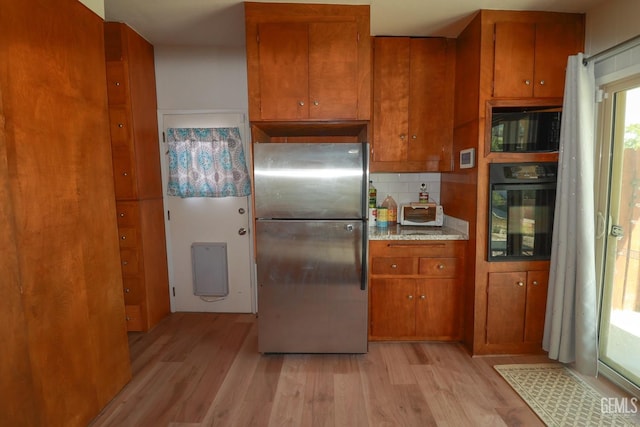 kitchen with black appliances, decorative backsplash, and light wood-type flooring