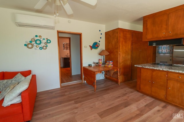 kitchen with a wall mounted air conditioner, light wood-type flooring, ceiling fan, electric cooktop, and stainless steel refrigerator